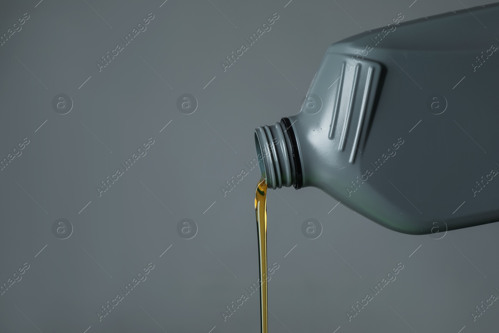 Pouring motor oil from canister on grey background, closeup. Space for text Photo of Pouring motor oil from canister on grey background, closeup. Space for text