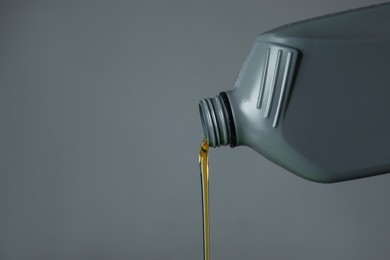 Photo of Pouring motor oil from canister on grey background, closeup. Space for text