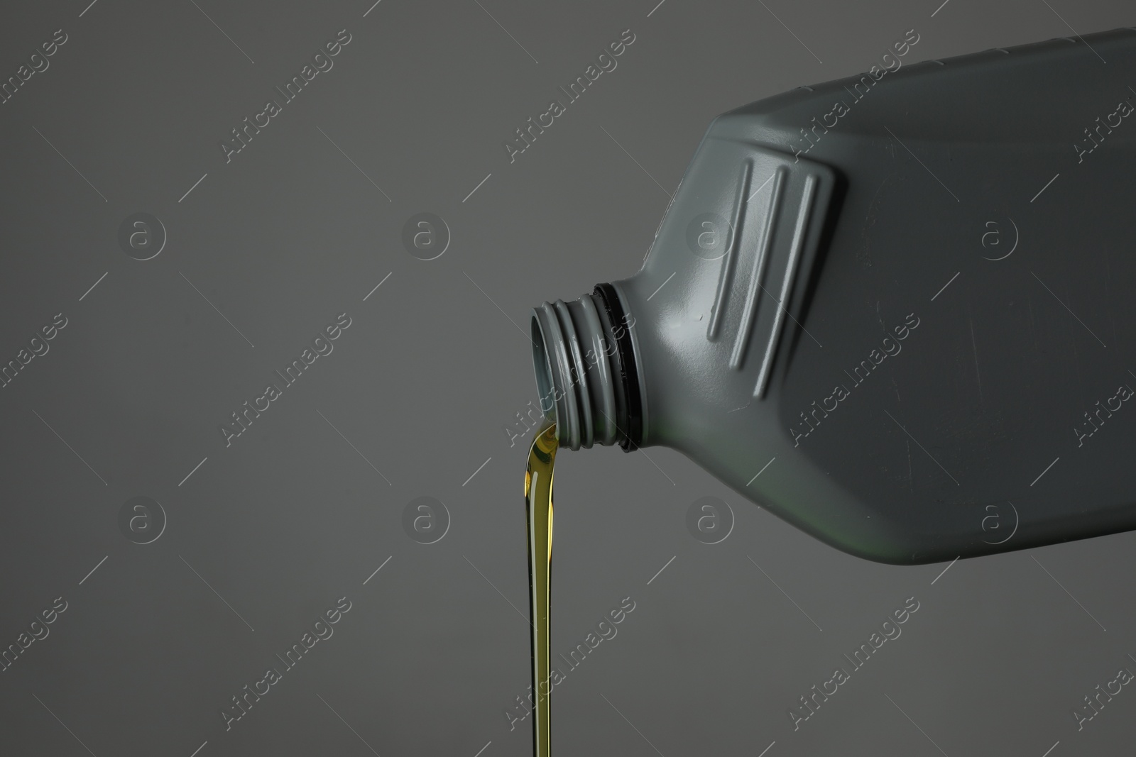 Pouring motor oil from canister on grey background, closeup. Space for text Photo of Pouring motor oil from canister on grey background, closeup. Space for text