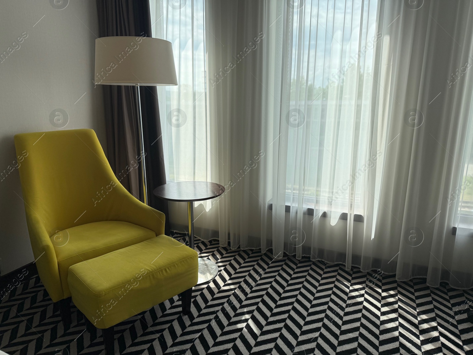 Yellow armchair, pouf, lamp and side table near window indoors. Interior design Photo of Yellow armchair, pouf, lamp and side table near window indoors. Interior design