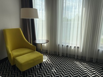 Photo of Yellow armchair, pouf, lamp and side table near window indoors. Interior design