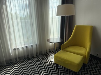 Photo of Yellow armchair, pouf, lamp and side table near window indoors. Interior design