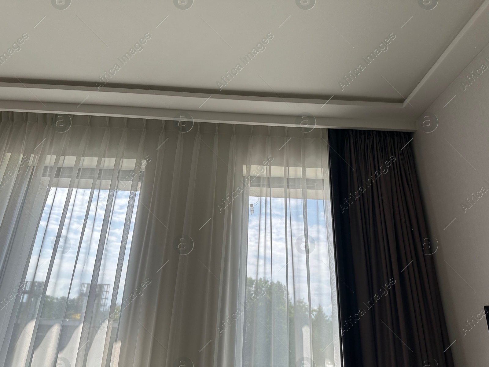 Beautiful curtains hanging on cornice near window indoors, low angle view Photo of Beautiful curtains hanging on cornice near window indoors, low angle view