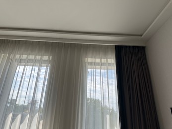 Photo of Beautiful curtains hanging on cornice near window indoors, low angle view