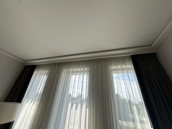 Photo of Beautiful curtains hanging on cornice near window indoors, low angle view