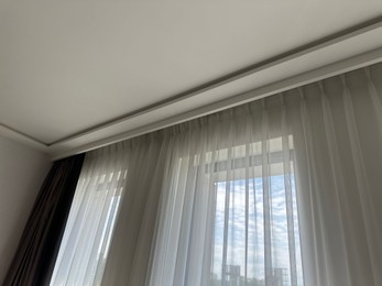 Photo of Beautiful curtains hanging on cornice near window indoors, low angle view