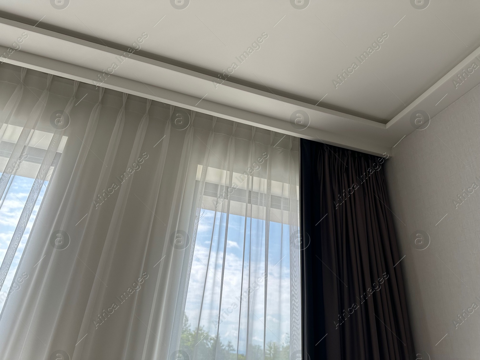 Beautiful curtains hanging on cornice near window indoors, low angle view Photo of Beautiful curtains hanging on cornice near window indoors, low angle view