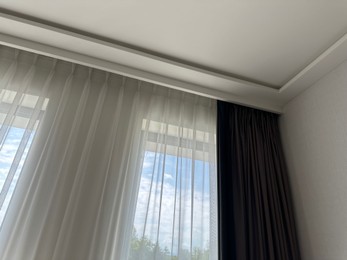 Photo of Beautiful curtains hanging on cornice near window indoors, low angle view