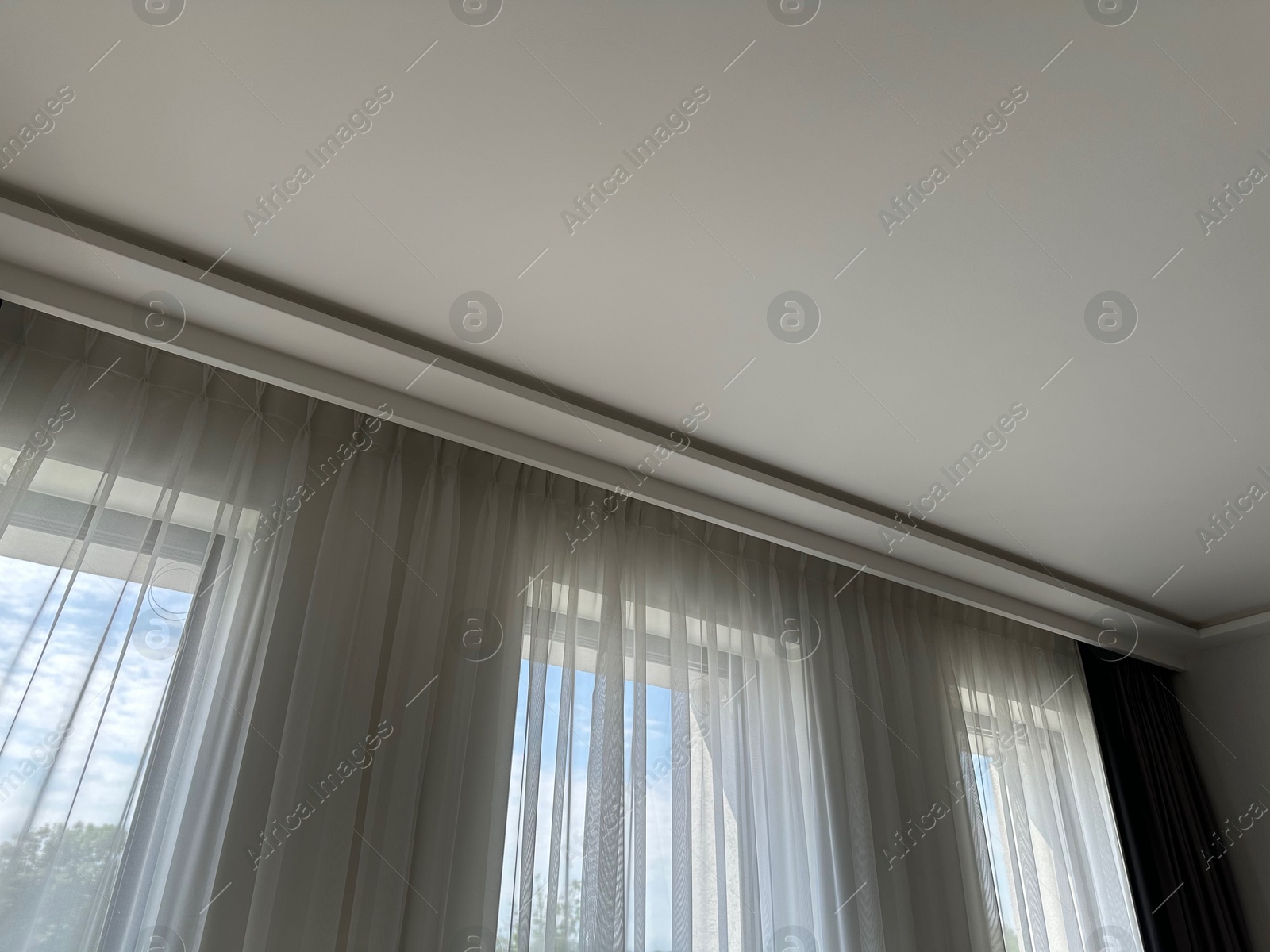 Beautiful curtains hanging on cornice near window indoors, low angle view Photo of Beautiful curtains hanging on cornice near window indoors, low angle view