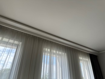 Photo of Beautiful curtains hanging on cornice near window indoors, low angle view