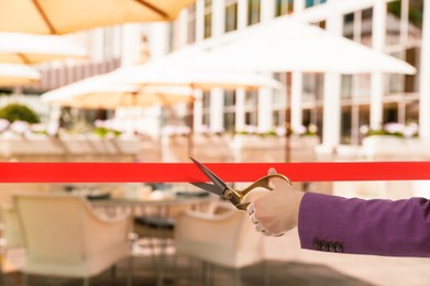 Image of Woman cutting red ribbon at opening ceremony of resort, closeup