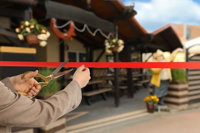 Image of Woman cutting red ribbon at opening ceremony of restaurant, closeup