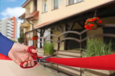 Image of Man cutting red ribbon at opening ceremony of restaurant, closeup