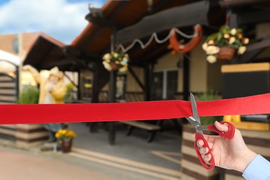 Image of Man cutting red ribbon at opening ceremony of restaurant, closeup