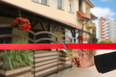 Image of Man cutting red ribbon at opening ceremony of restaurant, closeup