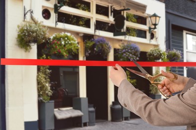 Image of Woman cutting red ribbon at opening ceremony of restaurant, closeup