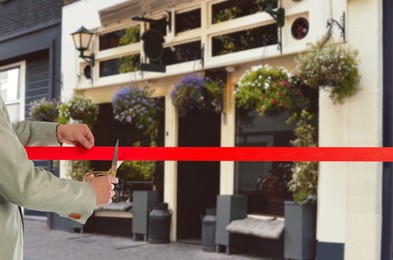 Image of Man cutting red ribbon at opening ceremony of restaurant, closeup