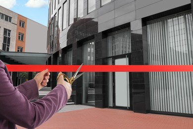 Image of Woman cutting red ribbon at opening ceremony of office building, closeup