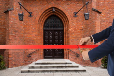 Image of Man cutting red ribbon at opening ceremony of house, closeup