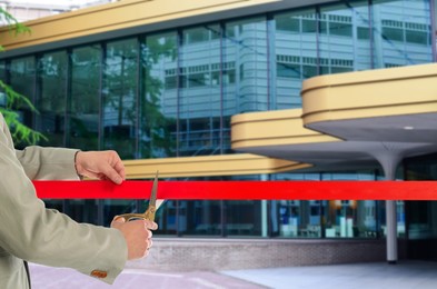 Image of Man cutting red ribbon at opening ceremony of hotel, closeup