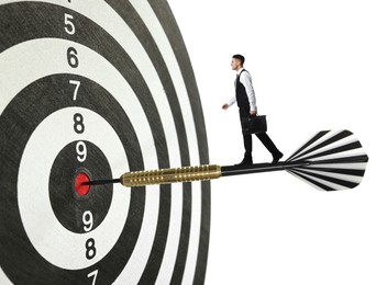 Image of Goal achievement, business success and targeting. Businessman walking on dart sticking in center of dartboard against white background