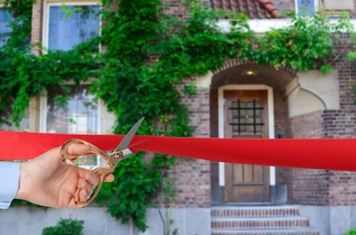 Image of Man cutting red ribbon at opening ceremony of housing estate, closeup