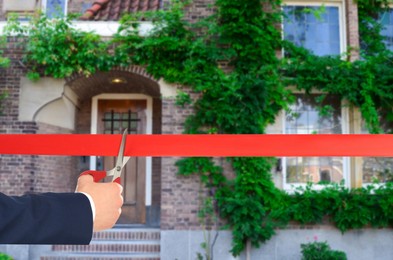 Image of Man cutting red ribbon at opening ceremony of housing estate, closeup