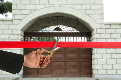 Image of Man cutting red ribbon at opening ceremony of house, closeup