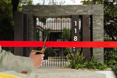 Image of Man cutting red ribbon at opening ceremony of house, closeup