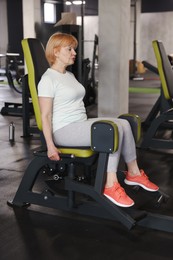 Photo of Senior woman training on seated hip abduction machine in gym
