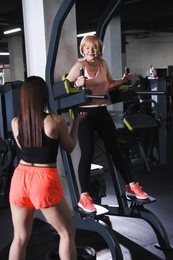 Photo of Senior woman training on power tower supervised by professional trainer in gym