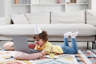 Photo of Birthday celebration. Little boy with piece of cake having video call via laptop at home. Space for text