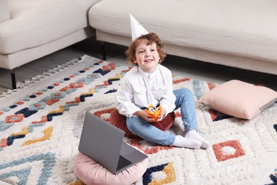 Photo of Birthday celebration. Little boy with cupcake having video call via laptop at home
