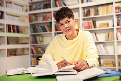 Photo of Student with books studying at table in library