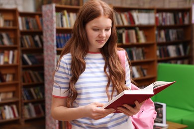 Photo of Student with book and backpack in library