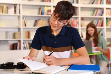 Photo of Student with books studying at table in library