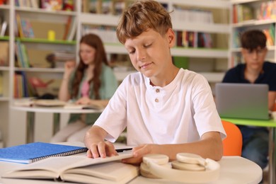 Photo of Student with books studying at table in library