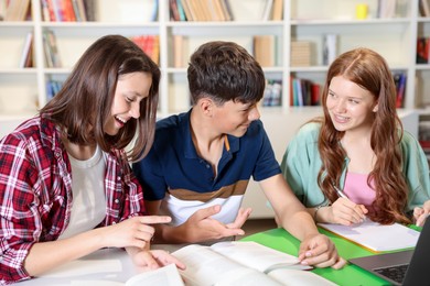 Photo of Students with books and laptop studying together at table in library