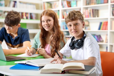 Photo of Students with books studying together at table in library