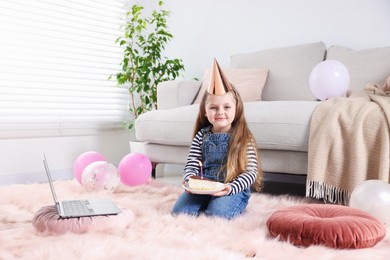 Photo of Birthday celebration. Little girl with piece of cake having video call via laptop at home
