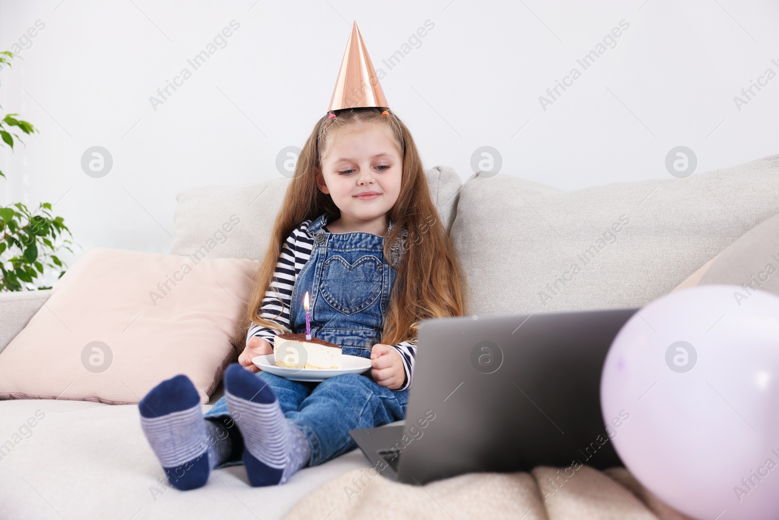 Birthday celebration. Little girl with piece of cake having video call via laptop on sofa at home Photo of Birthday celebration. Little girl with piece of cake having video call via laptop on sofa at home