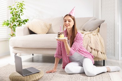 Photo of Birthday celebration. Happy woman with piece of cake having video call via laptop at home
