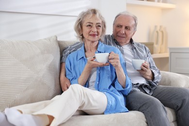 Photo of Lovely senior couple enjoying hot drinks on sofa at home