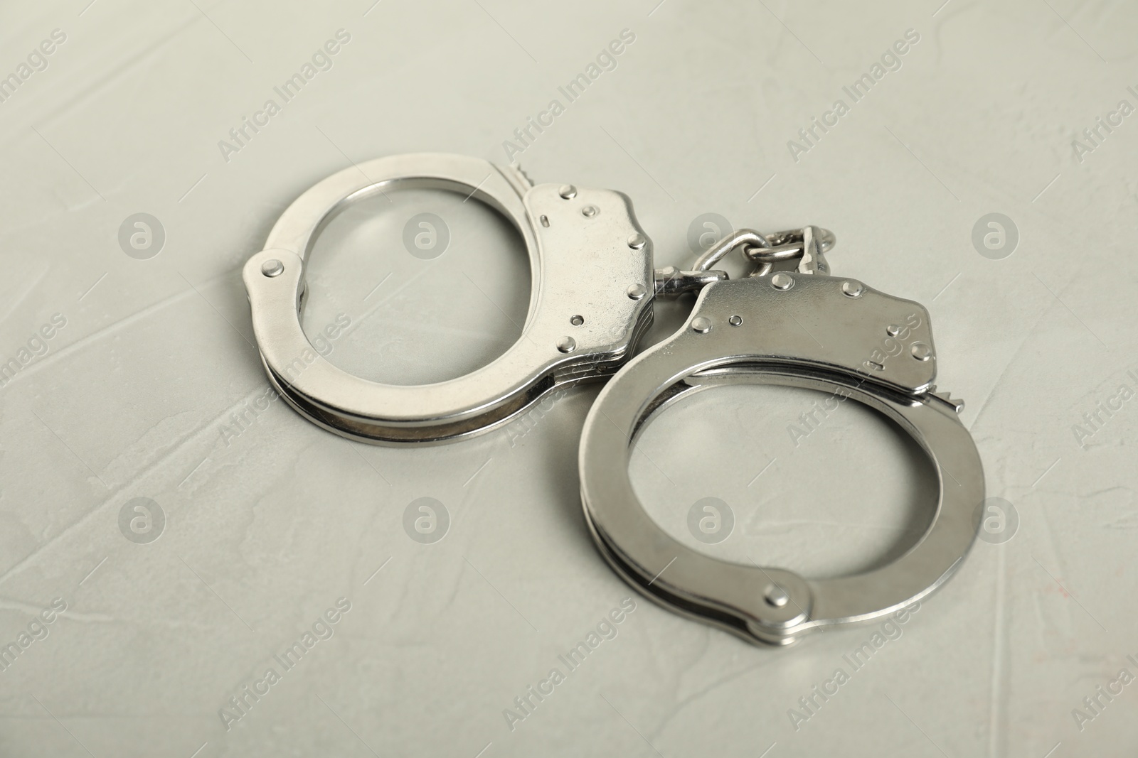 Handcuffs on light grey table, closeup. Police equipment Photo of Handcuffs on light grey table, closeup. Police equipment