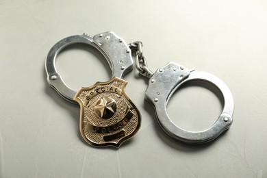Photo of Police badge and handcuffs on light grey table, above view