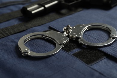Photo of Handcuffs and gun on bulletproof vest, closeup. Police equipment