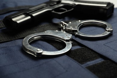 Photo of Handcuffs and gun on bulletproof vest, closeup. Police equipment