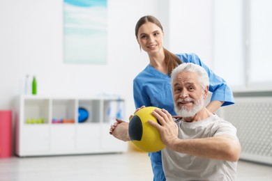 Photo of Doctor and patient exercising with medicine ball in clinic, space for text