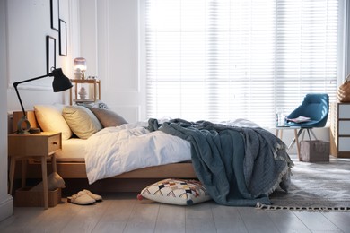 Photo of Cozy bed with soft linens, nightstand and lamp in stylish room. Home textile