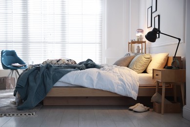 Photo of Cozy bed with soft linens, nightstand and lamp in stylish room. Home textile